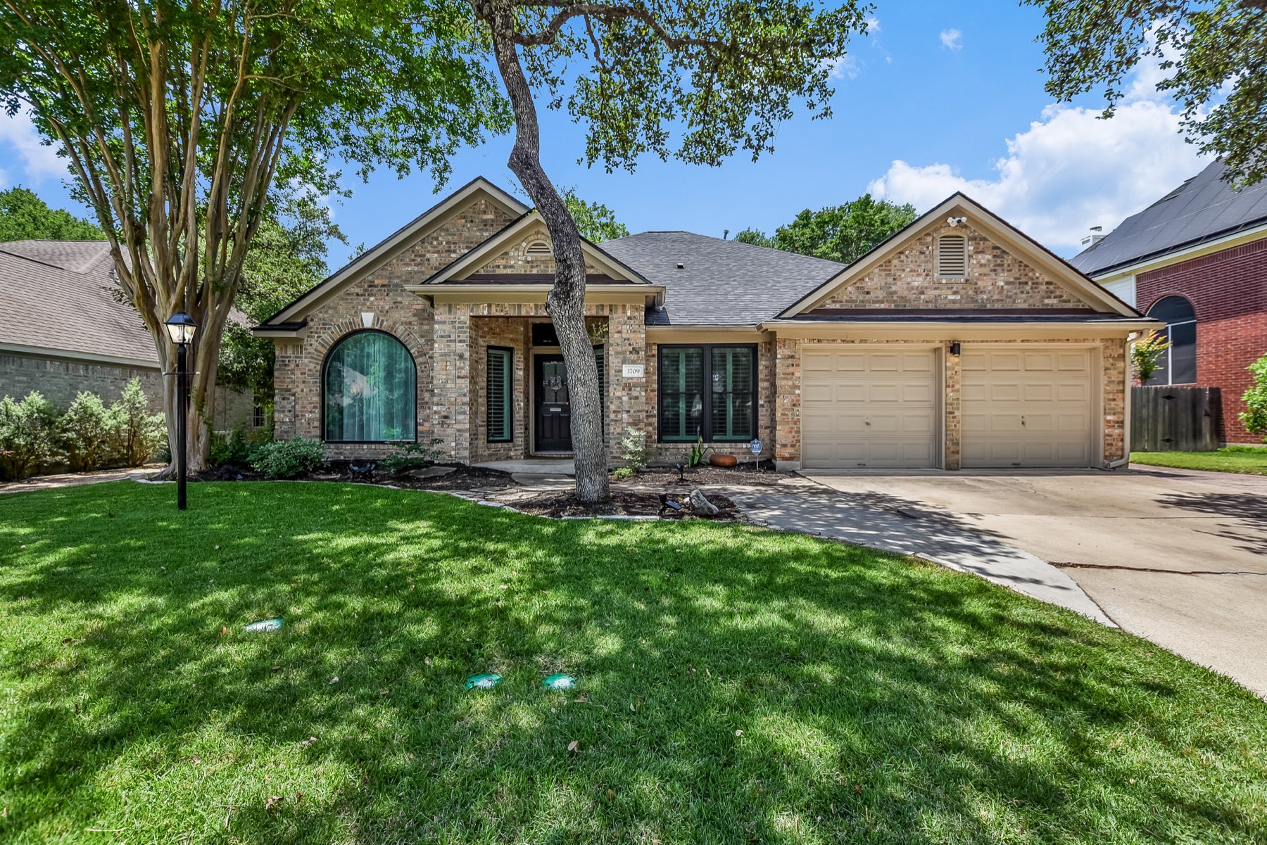 Brick single-story home with arched window, two-car garage and a large live oak in the front yard