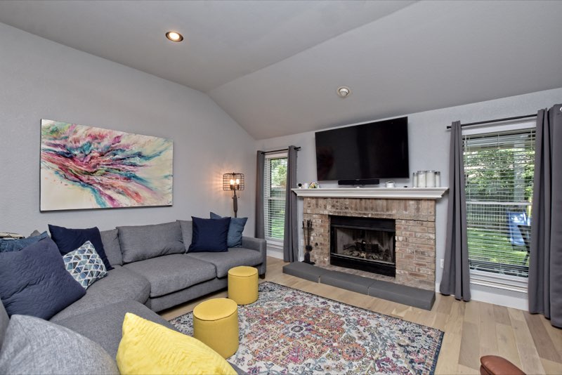 Family room with vaulted ceiling, brick fireplace with white mantel and tall windows
