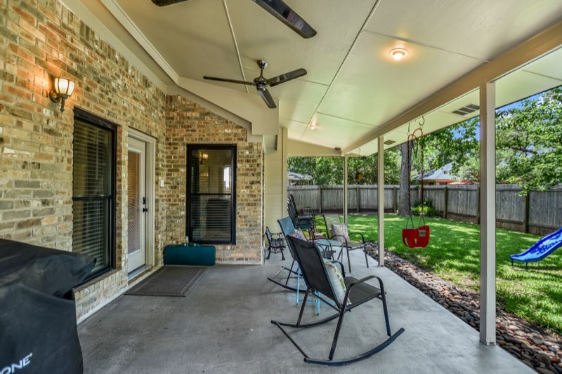 Long covered patio with two ceiling fans overlooking a green fenced backyard